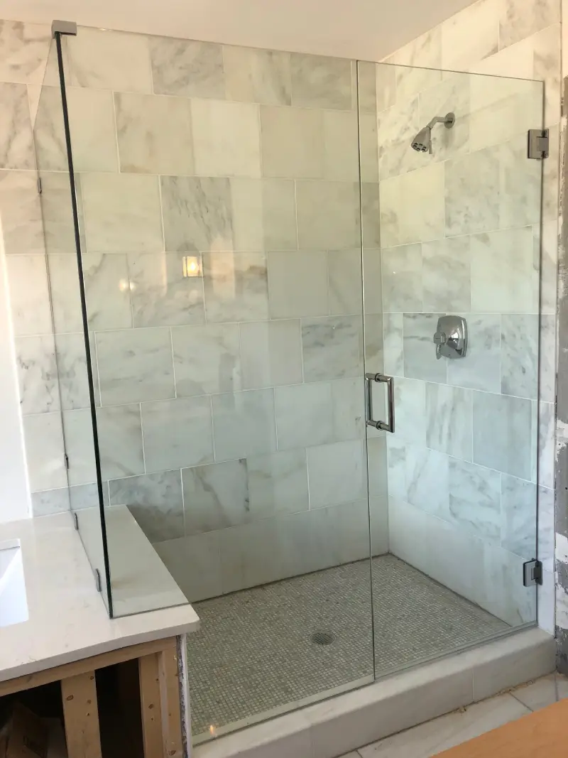 A bathroom with marble walls and floor, and a large glass shower.