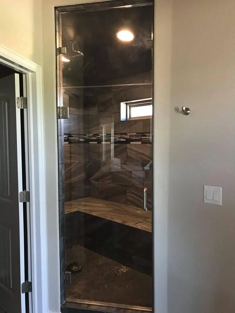 A walk in shower with glass doors and a wooden bench.